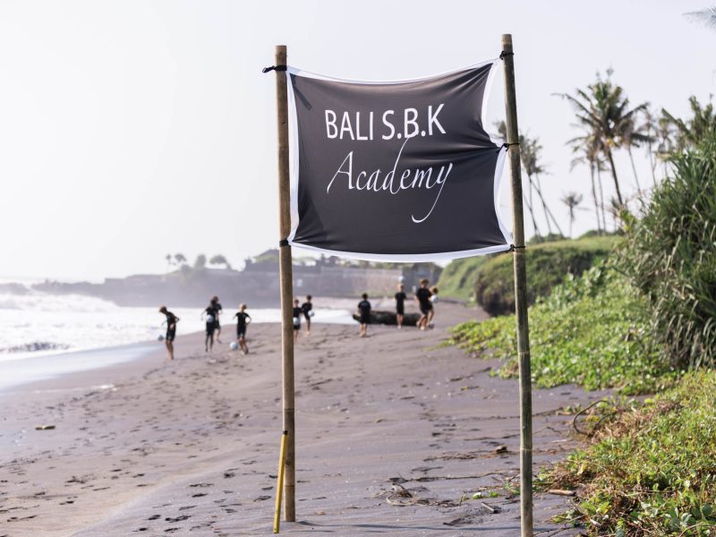 Team Bali SBK junior players train on beach, with football team's flag in foreground.